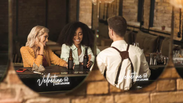 広島にて、バーに座っている人々の姿が、LEDロゴが施されたミラーに映し出されている様子のサムネイルです。